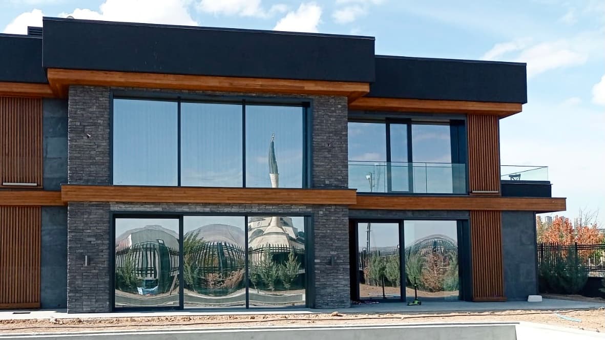 Close-up of stone and timber facade with floor-to-ceiling reflective glazing