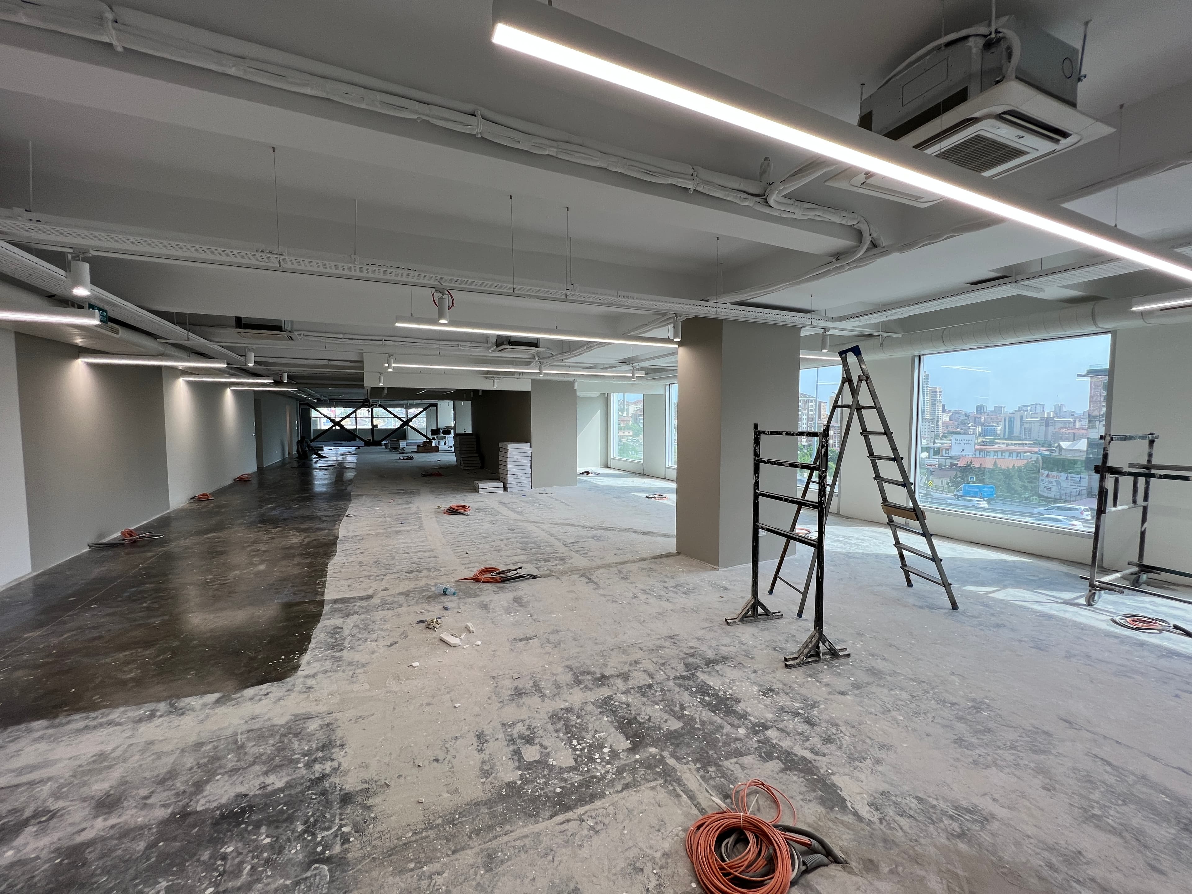 Construction site with ladders, exposed ceiling services, and city view through windows